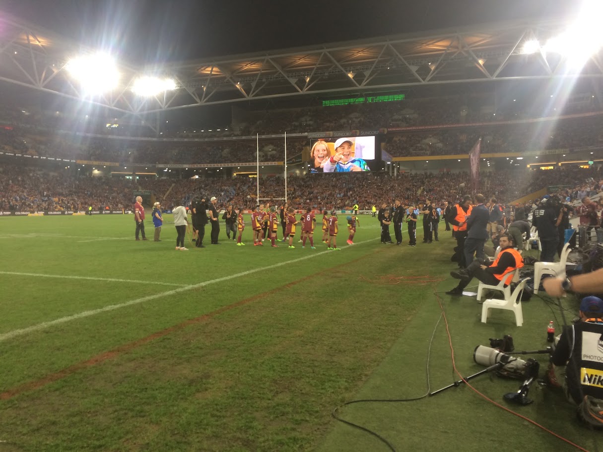 Floodlit rugby league stadium on Origin match night with a full crowd and junior players on the field